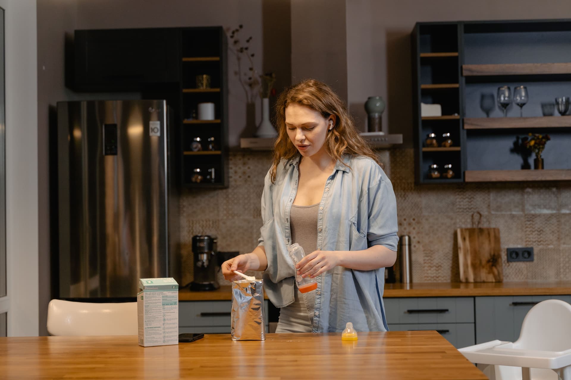 A parent preparing baby formula in a warmly lit kitchen (illustrative photo)
