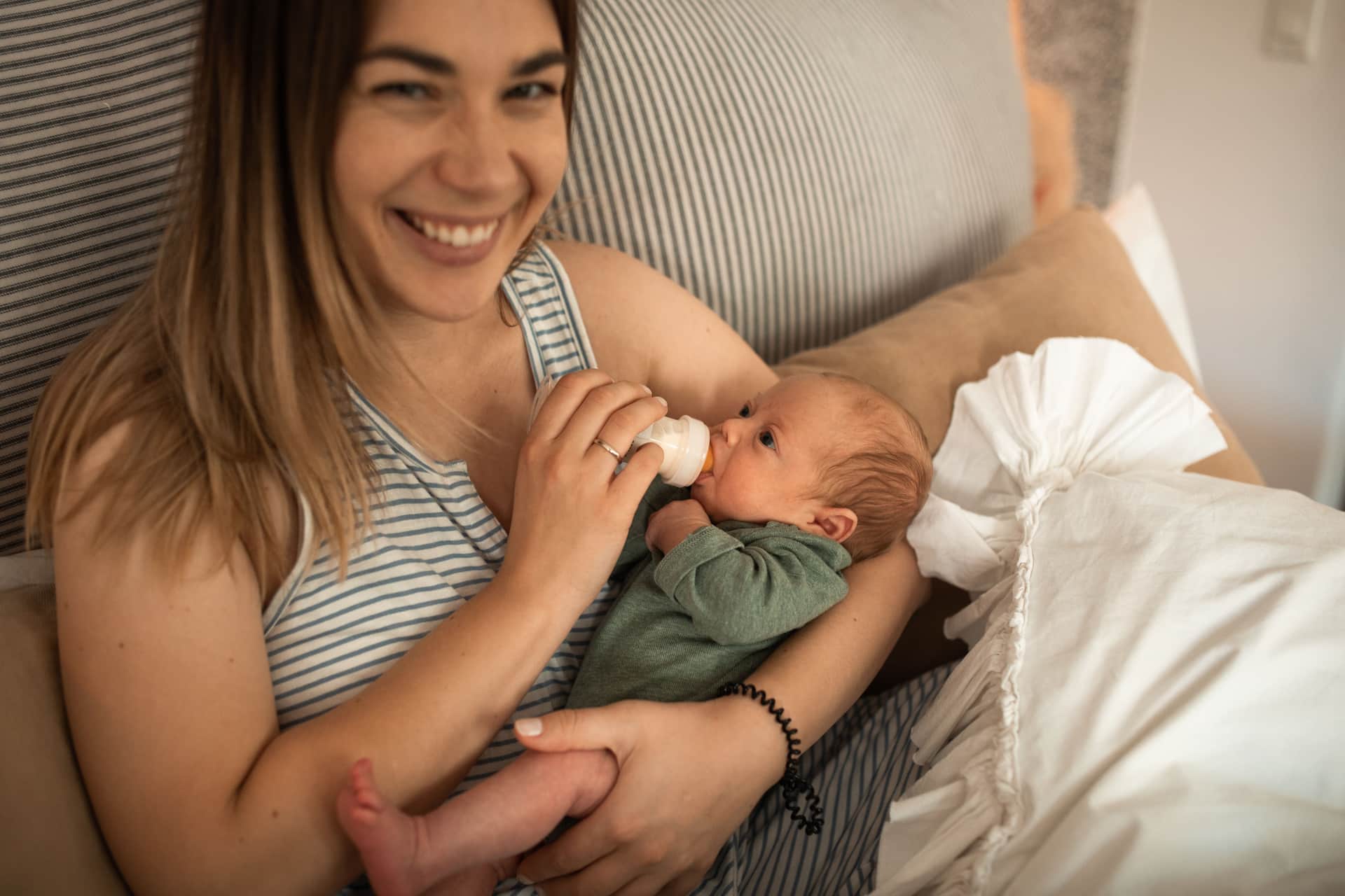 A parent smiling while feeding their newborn from a bottle (illustrative photo)