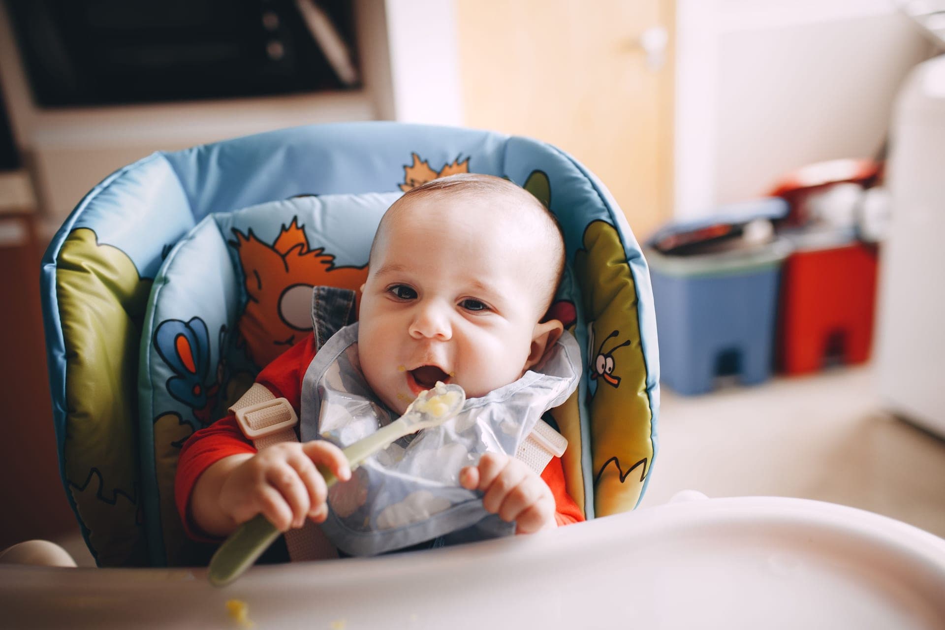 A baby in a feeding chair putting a spoonful of food into their mouth (illustrative photo)