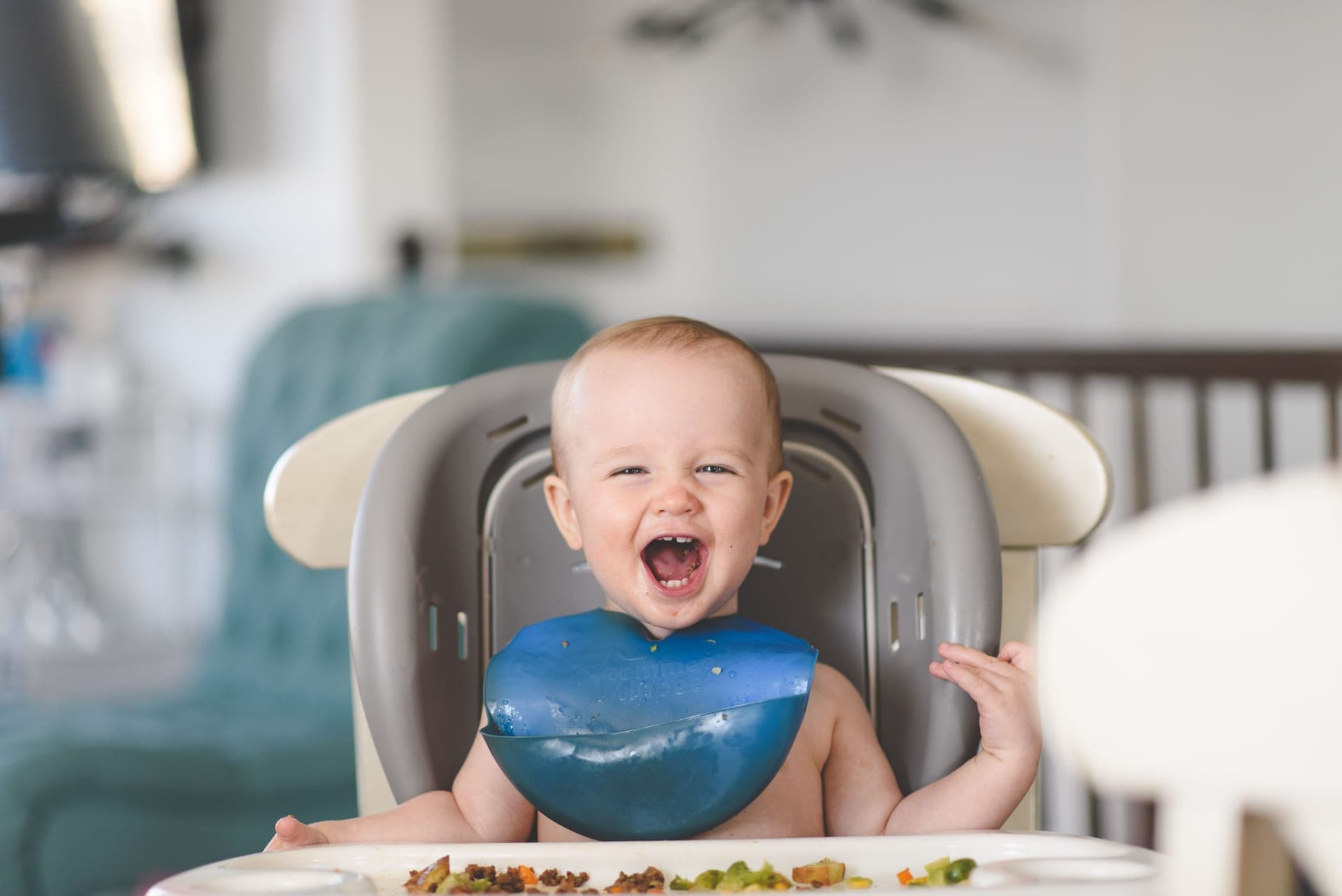 A baby laughing in a high chair at mealtime, wearing a bib (illustrative photo)