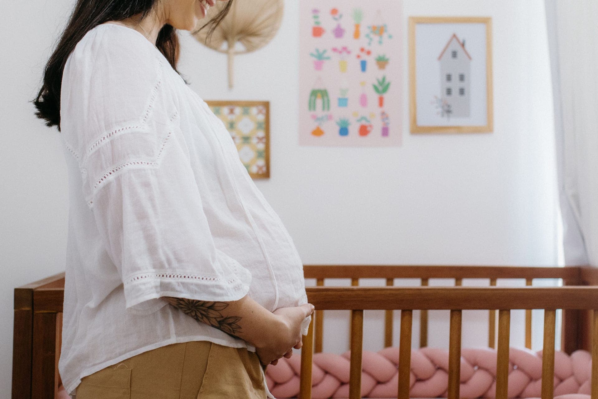 An expectant parent standing beside a wooden crib in a nursery (illustrative photo)