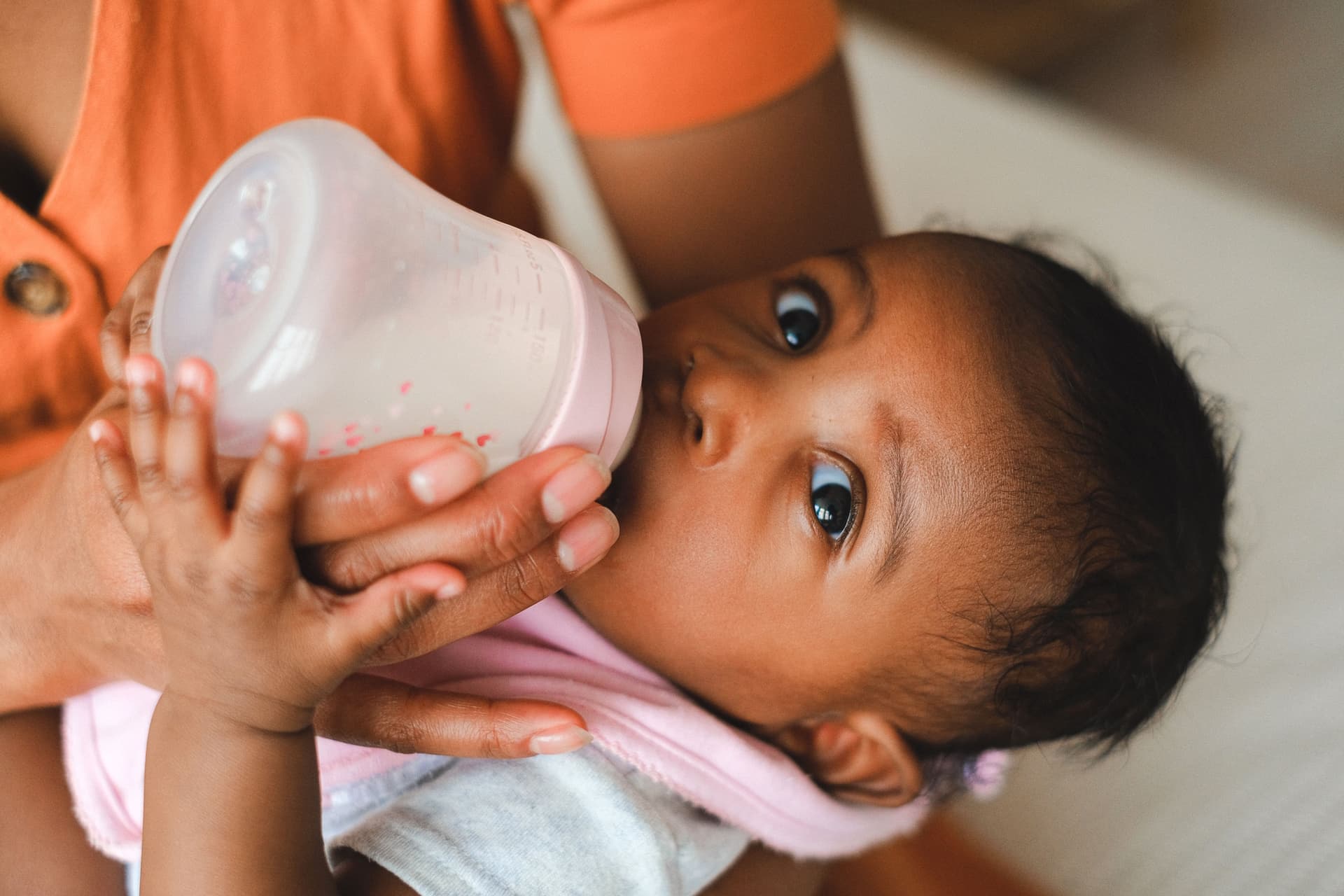 Close-up of a parent feeding their baby with a milk bottle indoors (illustrative photo)