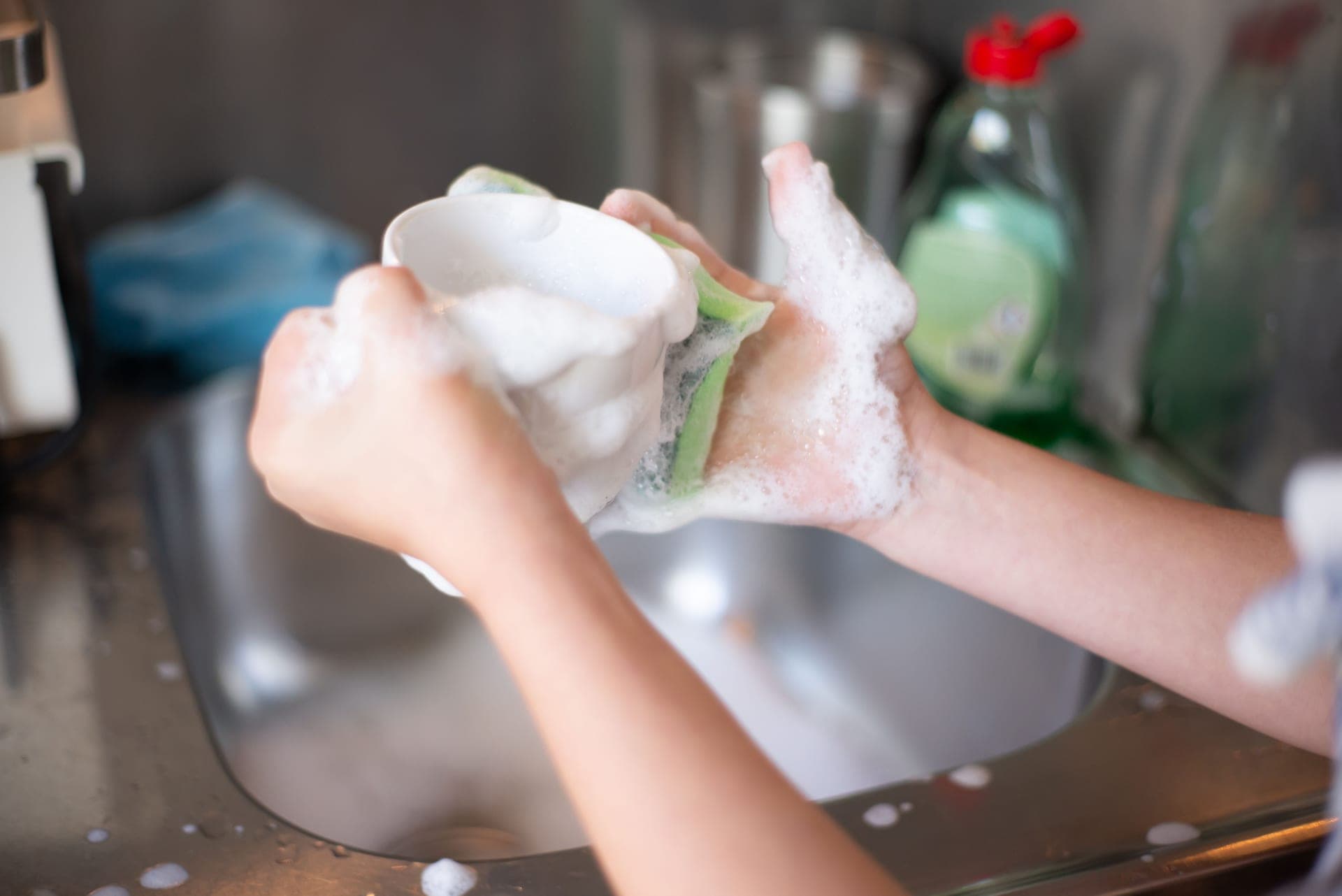 Hands washing a cup in soapy water at a kitchen sink (illustrative photo)